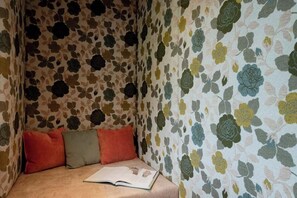 A corner of a room with floral patterned wallpaper, a beige sofa with three cushions, and an open book on the sofa. - Grappeskopf 23 Apartment (Gaschurn)