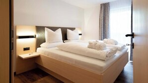 A hotel room with a bed, bedside tables, a headboard, and a window with curtains. - Grappeskopf 23 Apartment (Gaschurn)