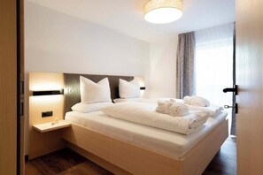 A hotel room with a bed, bedside tables, a headboard, and a window with curtains. - Grappeskopf 23 Apartment (Gaschurn)