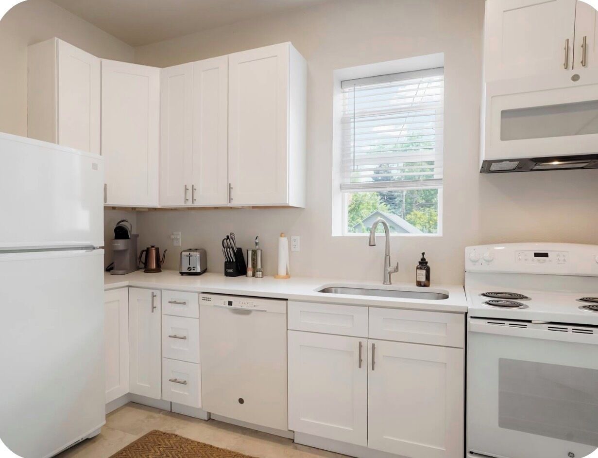 A kitchen with white cabinets, a built-in oven, a microwave, and a window with blinds.