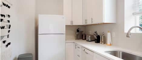 A modern kitchen with white cabinetry, a stainless steel sink, and a refrigerator.