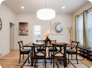 A dining area with a round table, six chairs, a vase with flowers, and a pendant light.