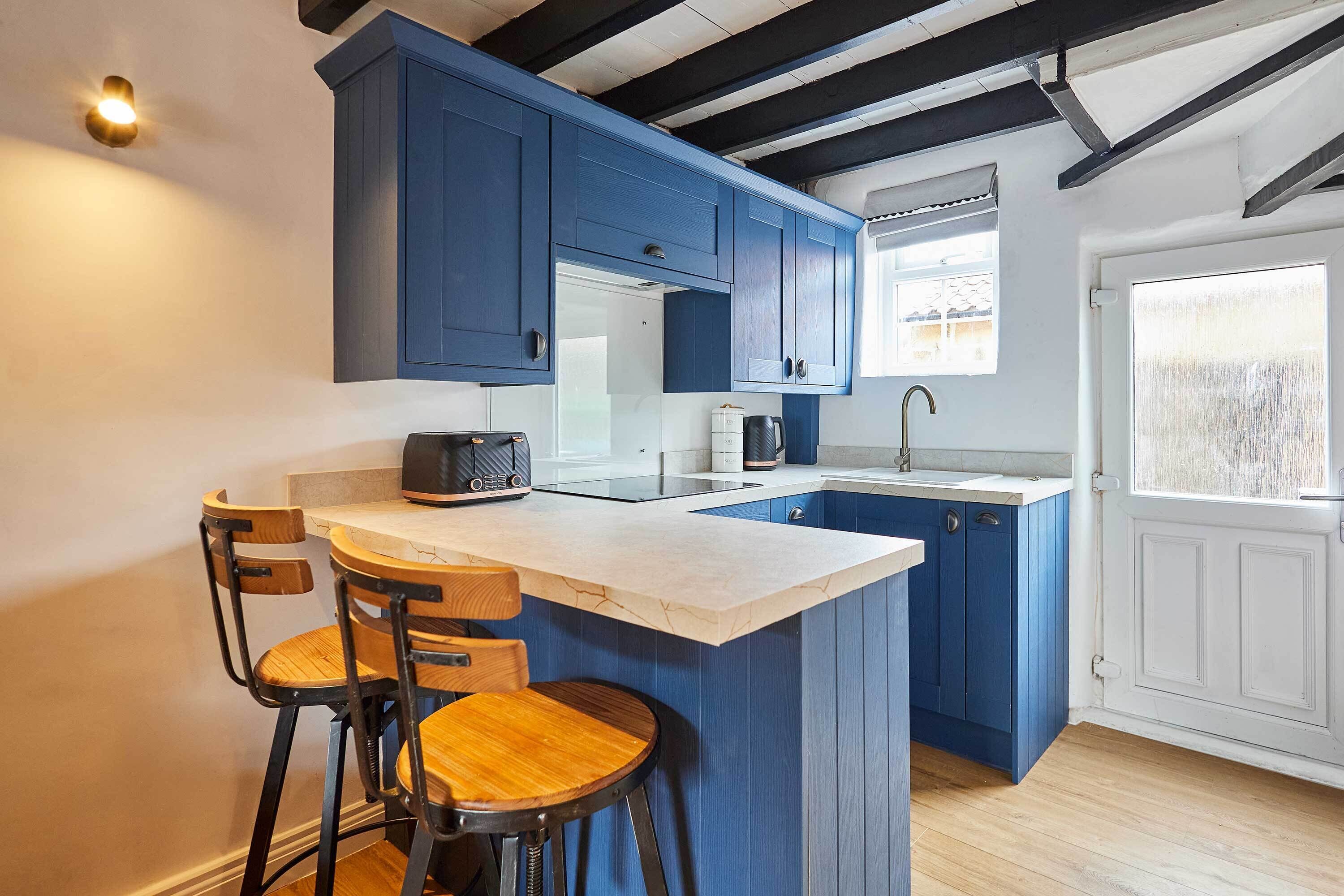 A kitchen with blue cabinets, a white countertop, a built-in island with stools, and a window with a view.