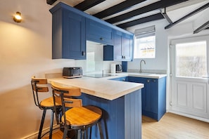 A kitchen with blue cabinets, a white countertop, a built-in island with stools, and a window with a view. - Host & Stay | Cuit's View (Great Ayton)