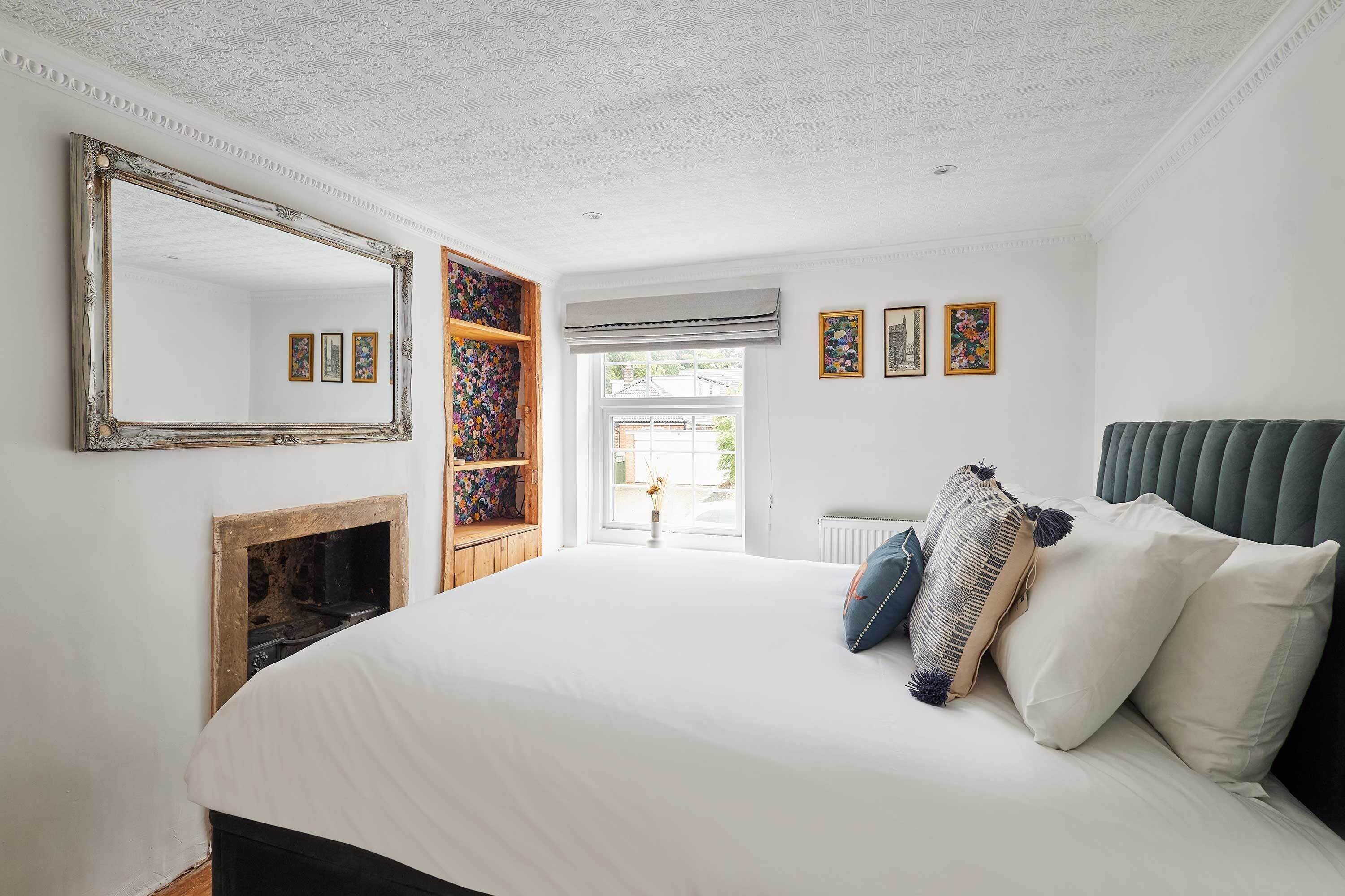 A bedroom with a large bed, a fireplace, a mirror, and a view of the outside.