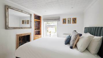 A bedroom with a large bed, a fireplace, a mirror, and a view of the outside.