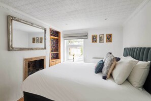 A bedroom with a large bed, a fireplace, a mirror, and a view of the outside.