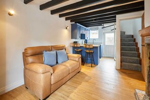 A living room with a brown leather sofa, a kitchen with blue cabinets, and a staircase. - Host & Stay | Cuit's View (Great Ayton)