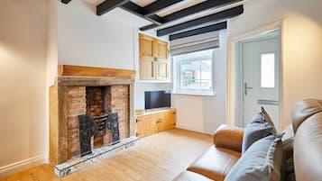 A living room with a fireplace, wooden beams, a television, and a sofa.