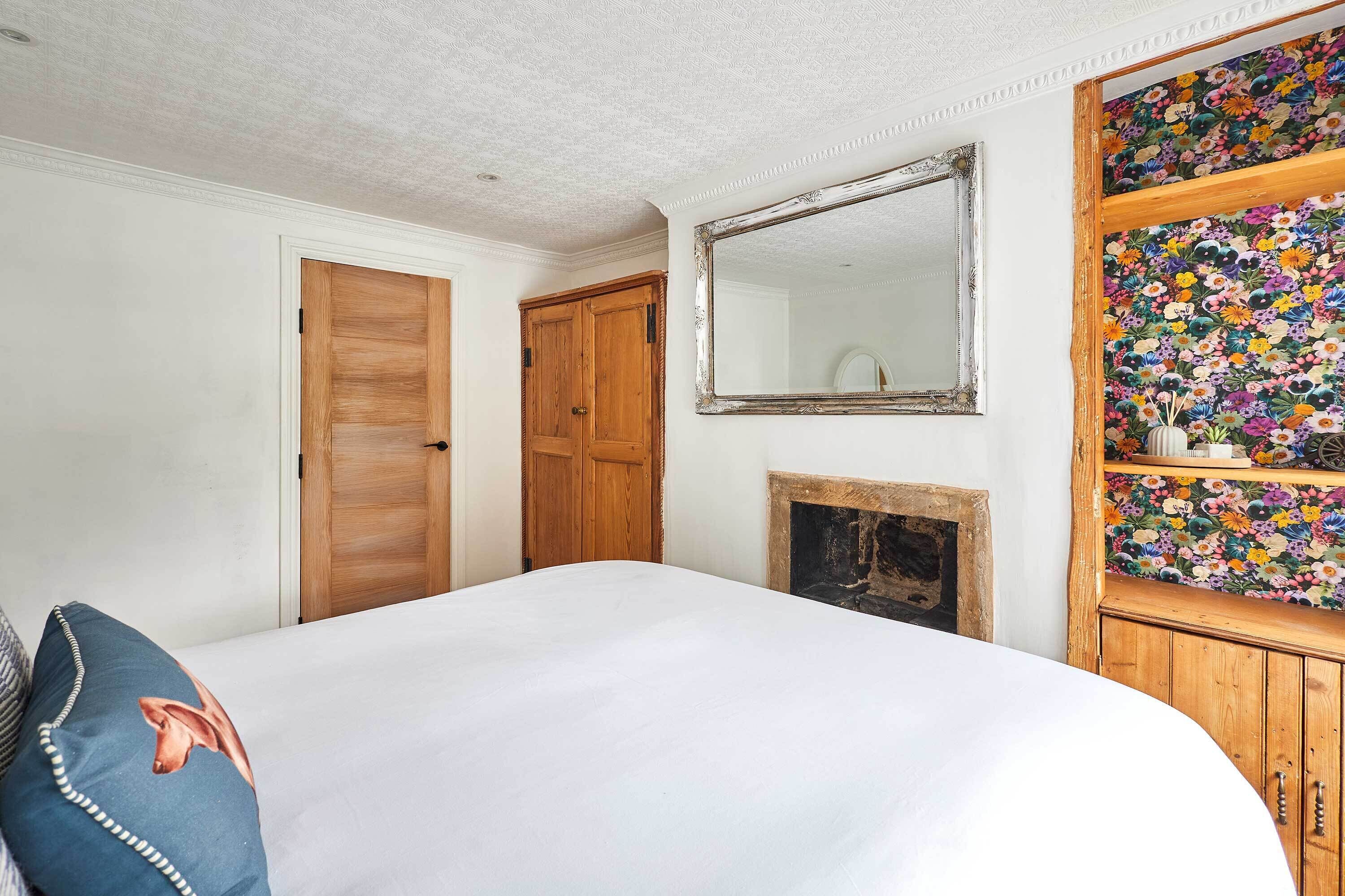 A bedroom with a wooden wardrobe, a mirror, a floral-patterned shelf, and a bed with a blue pillow.