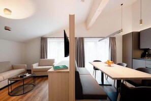 A modern living room with a sofa, a coffee table, a dining table with chairs, and a kitchen area with cabinets. - Madrisella 13 Apartment (Gaschurn)