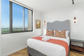 Quarto com uma janela grande, uma cama com roupa de cama branca e vista para uma paisagem.