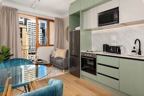 A modern kitchen with a Bosch oven, a microwave, and a sink. There is a dining table with chairs and a sofa in the living area. - Charlie and the Chairman | Designer Retreat (Cape Town)