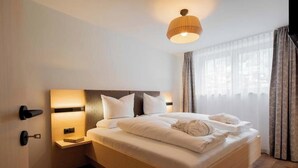 A hotel room with a large bed, bedside lamps, a nightstand, and a window with curtains. - Apartment Piz Buin 31 (Gaschurn)