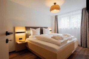 Ein Hotelzimmer mit einem großen Bett, Nachttischlampen, einem Beistelltisch und einem Fenster mit Vorhängen.