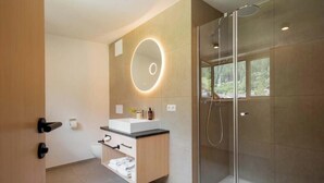 A modern bathroom with a glass shower enclosure, a round mirror with lighting, and a wooden vanity. - Apartment Piz Buin 31 (Gaschurn)