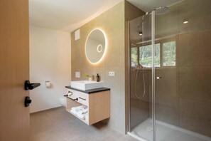Ein modernes Badezimmer mit einer Duschkabine aus Glas, einem runden Spiegel mit Beleuchtung und einem Holzwaschtisch.