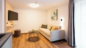 Ein modernes Wohnzimmer mit Sofa, Couchtisch, flachbildfernseher an der Wand und einem Fenster mit Vorhängen.