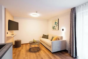 Ein modernes Wohnzimmer mit Sofa, Couchtisch, flachbildfernseher an der Wand und einem Fenster mit Vorhängen.