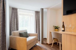 A modern living room with a sofa, a small table with a bottle and glasses, and a TV mounted on the wall. - Rifa E1 Apartment (Gaschurn)