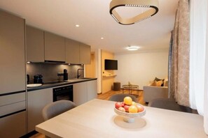 A modern kitchen with a dining area, a flat-screen TV, and a fruit bowl on the table. - Rifa E1 Apartment (Gaschurn)