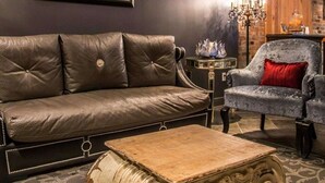 A leather sofa, a patterned armchair, a small table, and a decorative coffee table in a room with a brick wall and a chandelier.