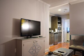 A living room with a flat-screen TV on a cabinet, a dining area with a table and chairs, and a kitchen with modern appliances.