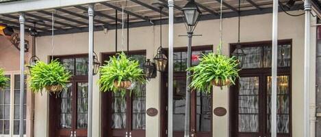 Un edificio con vestíbulo cubierto, plantas colgantes y barandilla de metal.