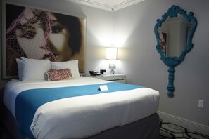 A hotel room with a large bed, a nightstand with a lamp, a mirror, and a wall with a large painting.