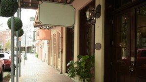 A sidewalk with a potted plant, a building entrance with a door, and a street with parked cars.