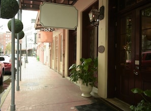 A sidewalk with a potted plant, a building entrance with a door, and a street with parked cars.