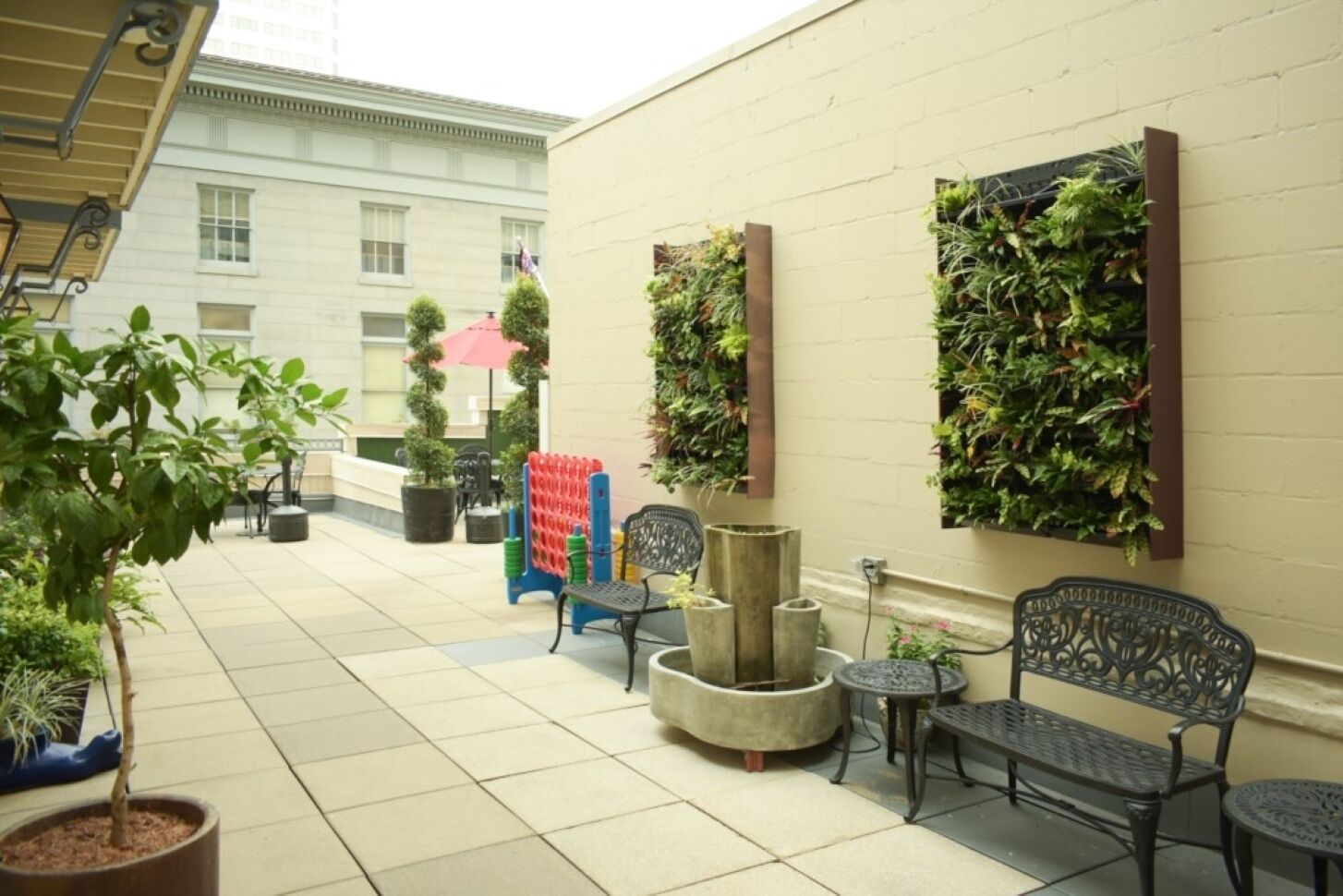 Un espace extérieur aménagé avec des chaises et des tables, un parasol rouge et des plantes en pot.