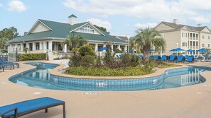 Un área de piscina con sillones de descanso, un pequeño jardín y un edificio con techo verde.