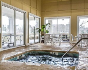 Una piscina cubierta climatizada con vistas al exterior, rodeada de sillas blancas y una planta en maceta.