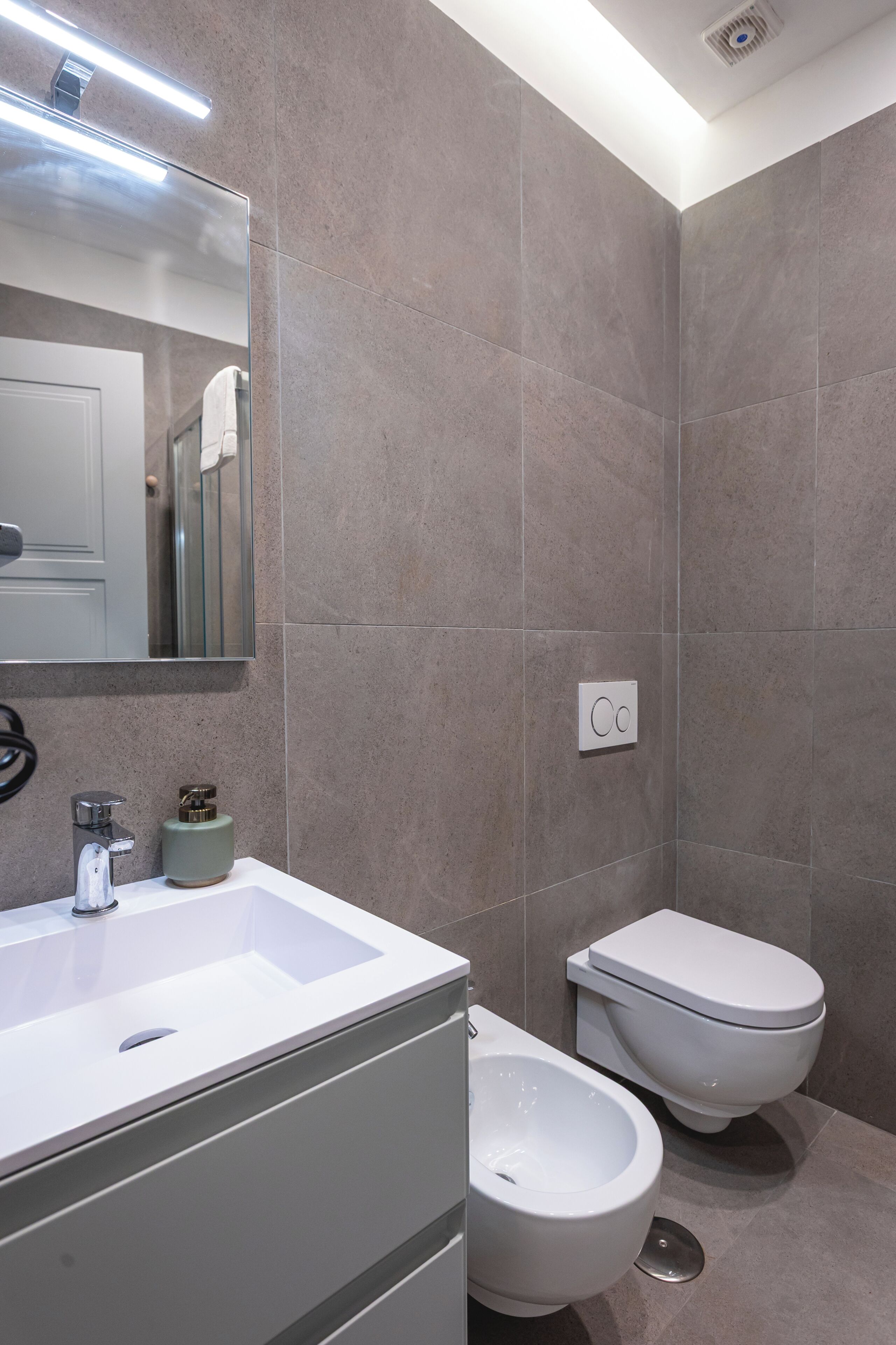 A modern bathroom with a large mirror, a sink, a bidet, and a toilet.