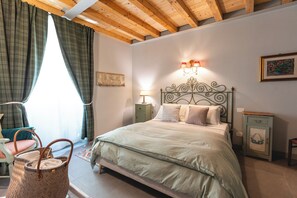 A bedroom with a bed, a nightstand, a lamp, a chair, and a window with curtains. - Palazzo San Biagio – In the heart of Viterbo’s historic center (Viterbo)