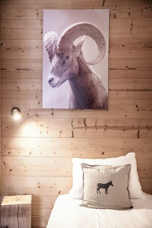 A bedroom with a wooden headboard, a bed with white bedding, a pillow with a donkey design, and a wall-mounted poster of a ram. - Cima – Balcony | Ski Locker | Parking | Morzine (Morzine)