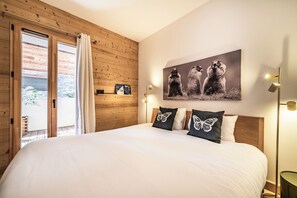Une chambre à coucher avec un grand lit, des murs en bois, une fenêtre avec des rideaux, un tableau accroché au mur et des lampes de chevet.