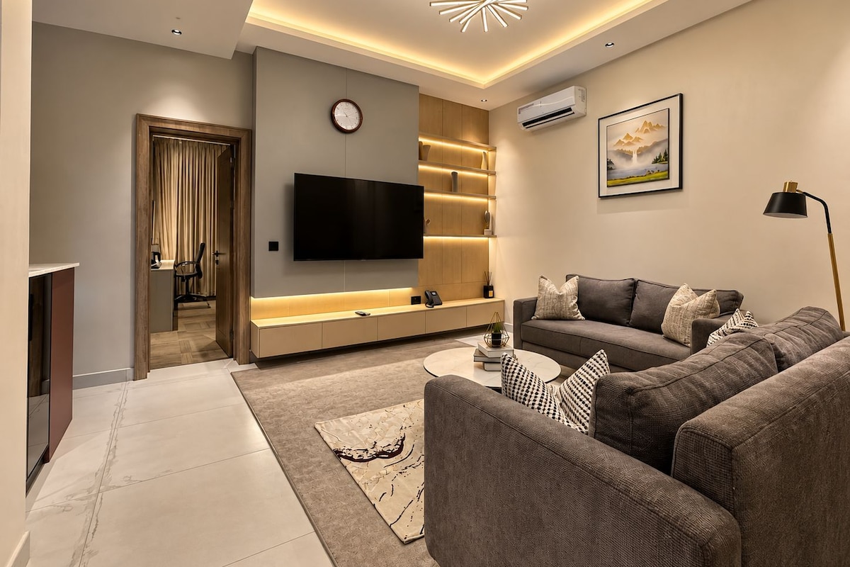 Ein modernes Wohnzimmer mit Flachbildfernseher, einer Couch, einem Couchtisch und einem dekorativen Teppich.