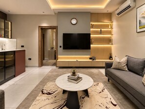 A modern living room with a sofa, a coffee table, and a TV mounted on the wall. - Rubis Signature Suites (Abuja)
