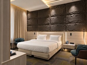 A modern hotel room with a large bed, a nightstand, a chair, and a textured wall. - Rubis Signature Suites (Abuja)