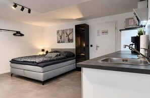 Un dormitorio moderno con cama, mesita de noche y una pequeña zona de escritorio con lavamanos.