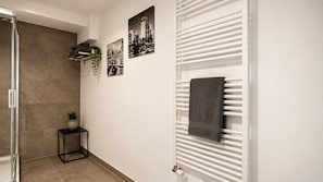 Een badkamer met een douche, een handdoekhouder en twee ingelijste foto's aan de muur.