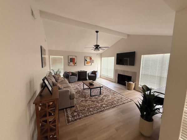 Una sala de estar con un conjunto de sofá, una mesa de centro, una chimenea y un televisor montado en la pared.