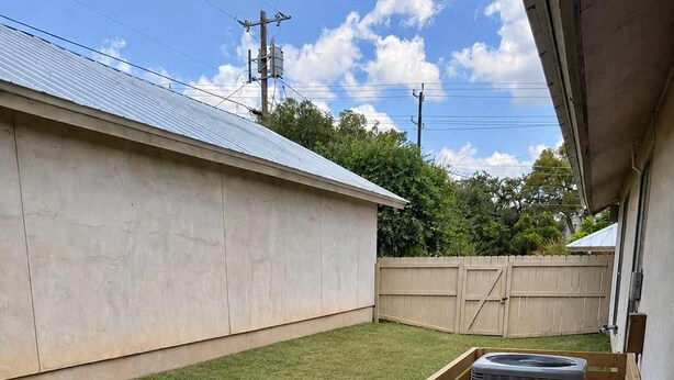 Ein Garten mit einer Holzterrasse, einem kleinen Baumstumpf und einer Betonmauer.