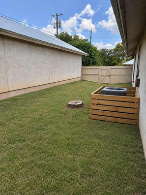 A backyard with a wooden deck, a small tree stump, and a concrete wall. - Tahoka Flats, Boutique Luxury Near Trinity & Pearl (San Antonio)