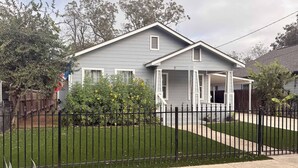 A residential house with a front porch, a fenced yard, and a well-maintained lawn. - 4BR Near Alamodome & Pearl | Sleeps 10 (San Antonio)