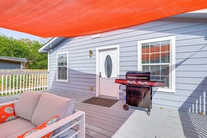 Een overdekt terras met een barbecue, een witte deur en een raam met zonwering.