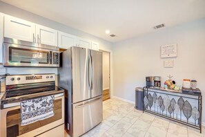 Una cocina moderna con electrodomésticos de acero inoxidable, muebles de cocina blancos y un estante decorativo con motivos de hojas.