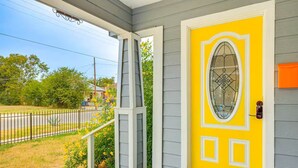 A house with a yellow door, a porch, and a fenced yard. - 4BR Near Alamodome & Pearl | Sleeps 10 (San Antonio)